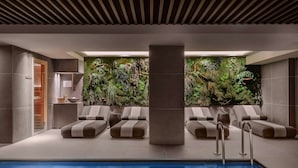A modern indoor pool area with lounge chairs, a large pillar, and a wall of greenery. - Radisson Collection Bilbao (Bilbao)