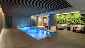A modern indoor pool area with a clear water feature, a lounge area with seating, and a wall with a green plant display. - Radisson Collection Bilbao (Bilbao)