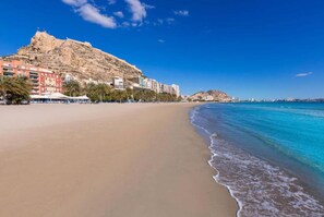 Une plage avec une montagne en arrière-plan, une eau d’un bleu limpide et des bâtiments qui bordent le rivage.
