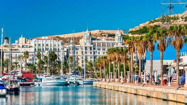 Un puerto deportivo con barcos, un paseo marítimo y edificios históricos.