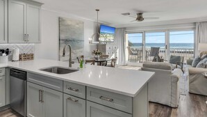 A modern kitchen with a large island, a dining area with a view of the ocean, and a balcony with a view of the beach.