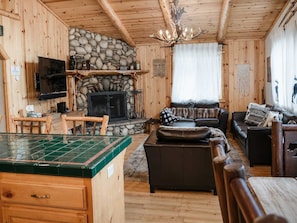 A wooden interior with a stone fireplace, a television, a sofa, and a dining area. - Four Happy Bears | AC, Hot Tub, EV| Walk to Summit (Big Bear Lake)