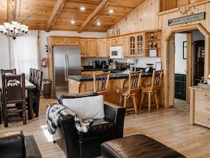 Interior de una cabaña con comedor, cocina y sala de estar con sofá y sillas.