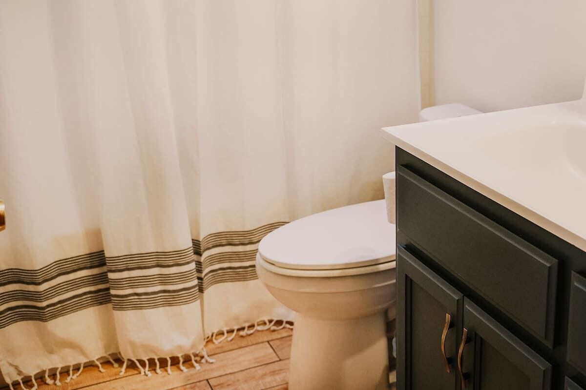 Un baño con inodoro blanco, un armario de madera oscura y una cortina de ducha a rayas.