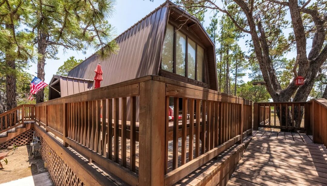 A cabin with a wooden deck and a metal roof, surrounded by trees.