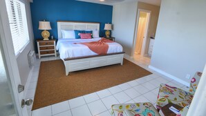Een slaapkamer met een bed, nachtkastjes, een plafondventilator en een deur naar een andere kamer.