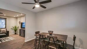 A modern living room with a dining area, featuring a ceiling fan, a flat-screen TV, and a wooden dining table with chairs. - Remodeled Tempe Home in Prime Location! (Tempe)
