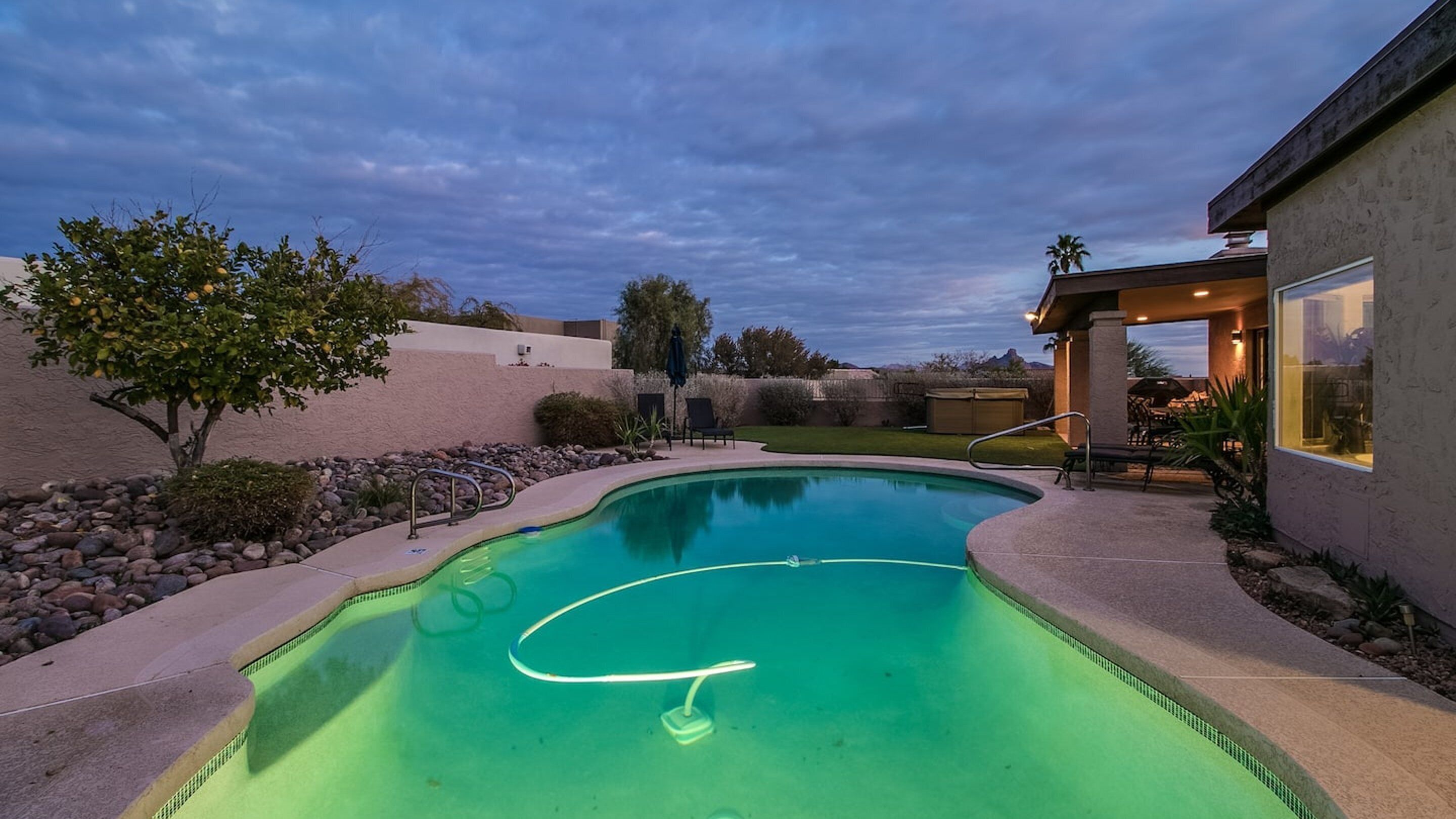 Une piscine à bord incurvé, entourée d’une terrasse dallée et d’un petit espace patio aménagé avec du mobilier d’extérieur.