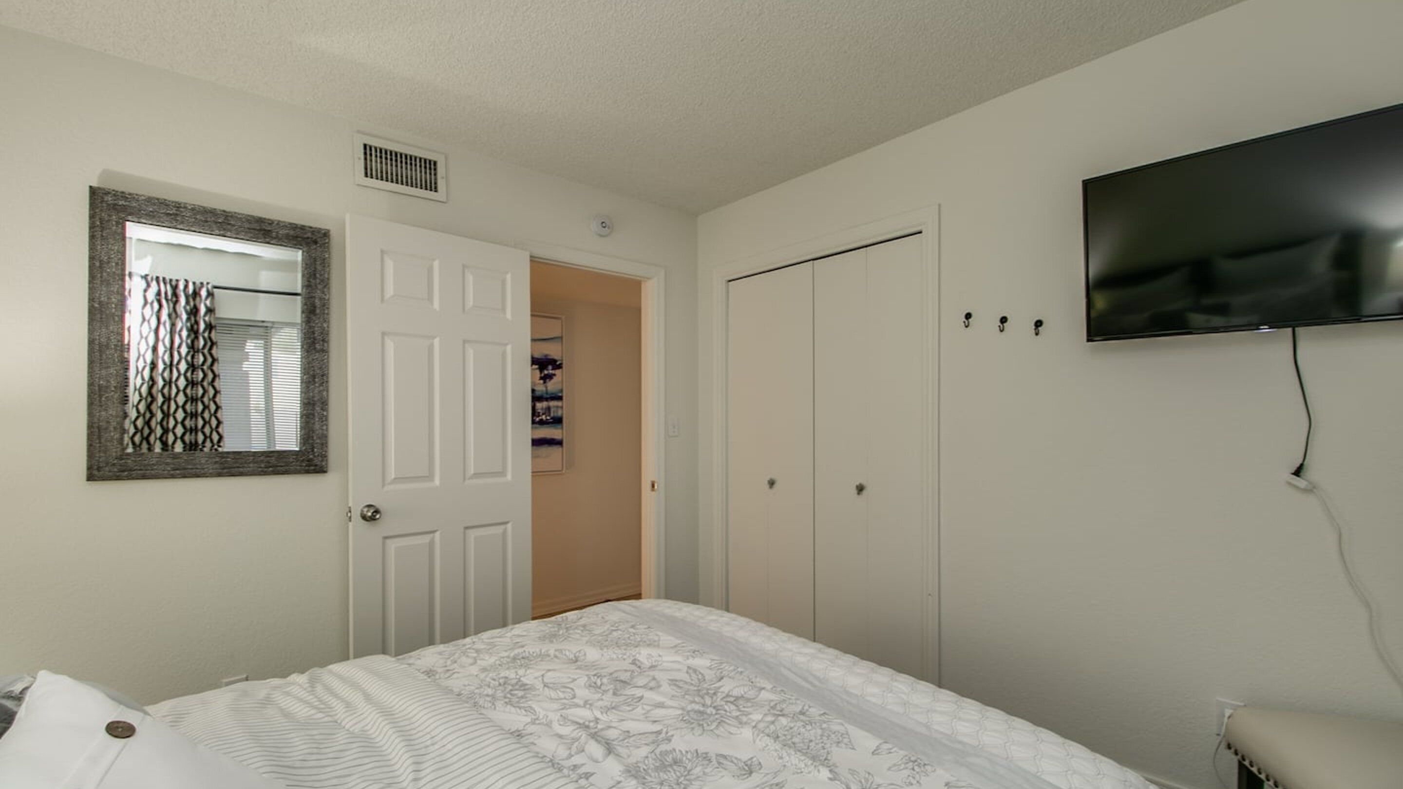 A bedroom with a bed, a wardrobe, a television mounted on the wall, and a door leading to another room.
