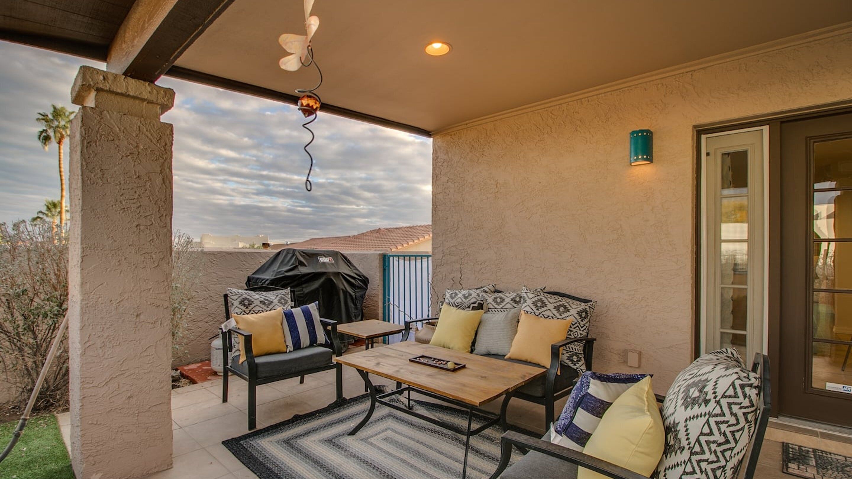 Eine Terrasse im Freien mit Tisch und Stühlen, einem überdachten Grill und Blick auf die Landschaft.