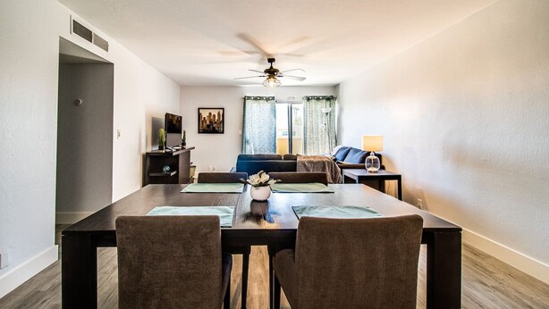 A dining area with a dark wooden table, two chairs, a ceiling fan, and a view of a living room with a sofa and a TV.