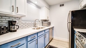 A modern kitchen with white cabinets, blue drawers, a stainless steel refrigerator, a microwave, and a coffee maker.