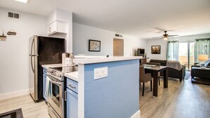 A modern kitchen with a central island, a dining area with a table and chairs, and a living room with a sofa and a TV.