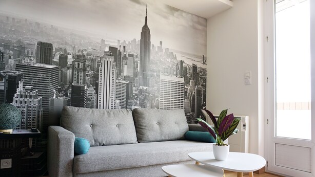 Ein Wohnzimmer mit grauem Sofa, einem kleinen weißen Tisch und einer Topfpflanze.