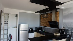Eine moderne Küche mit Einbaukühlschrank, Mikrowelle und Kaffeemaschine. Die Rückwand ist mit einem Holz-Fischgrätmuster versehen und durch das Fenster ist eine Stadtsicht zu sehen.
