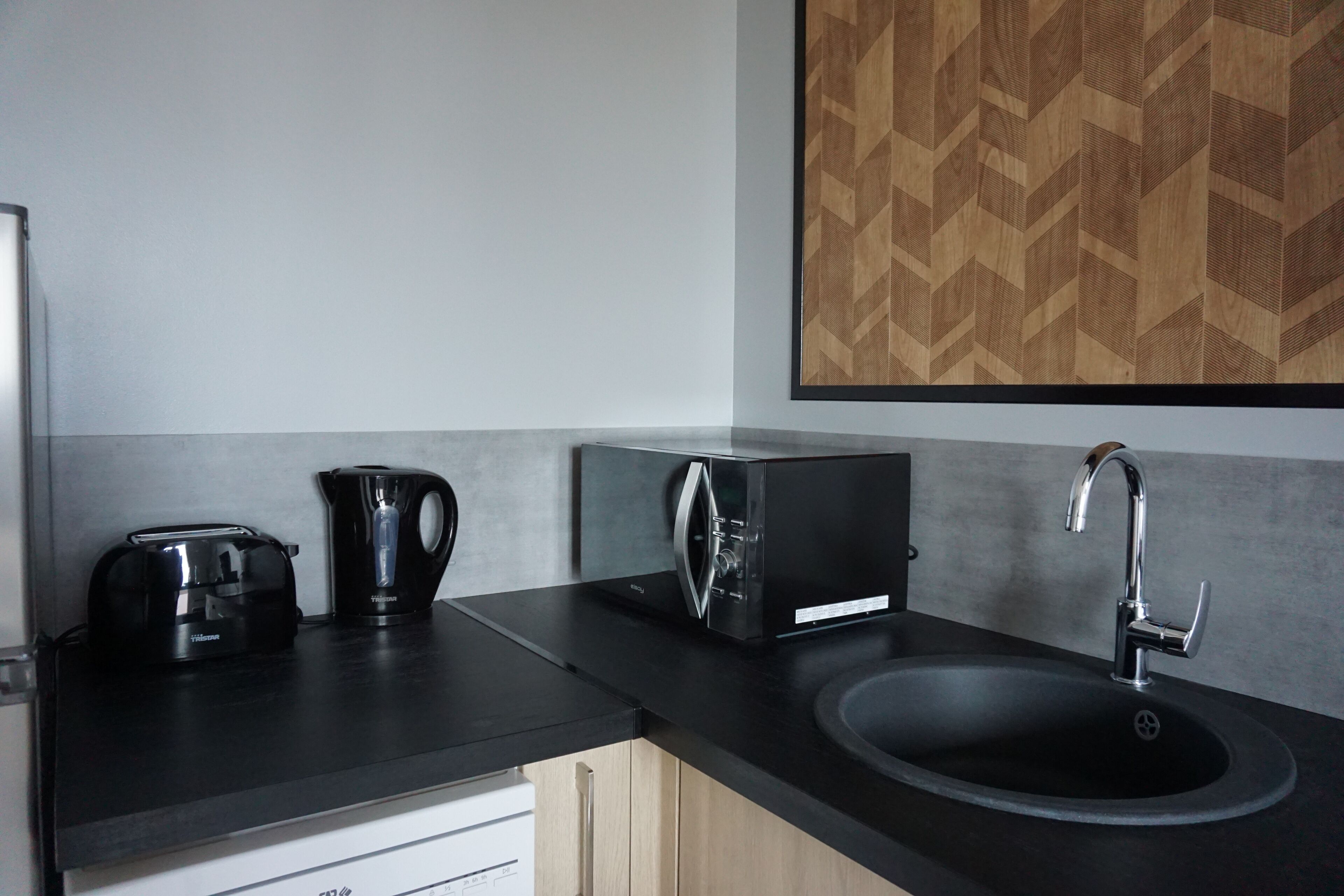 A modern kitchen with a black countertop, a sink, a kettle, and a microwave.