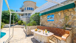 A stone-tiled outdoor seating area with a pool, a stone wall with a mural, and a tower in the background.
