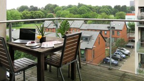 A balcony with a table, chairs, a laptop, a potted plant, and a newspaper. - Tudors eSuites Two Bedroom & Balcony (Birmingham)