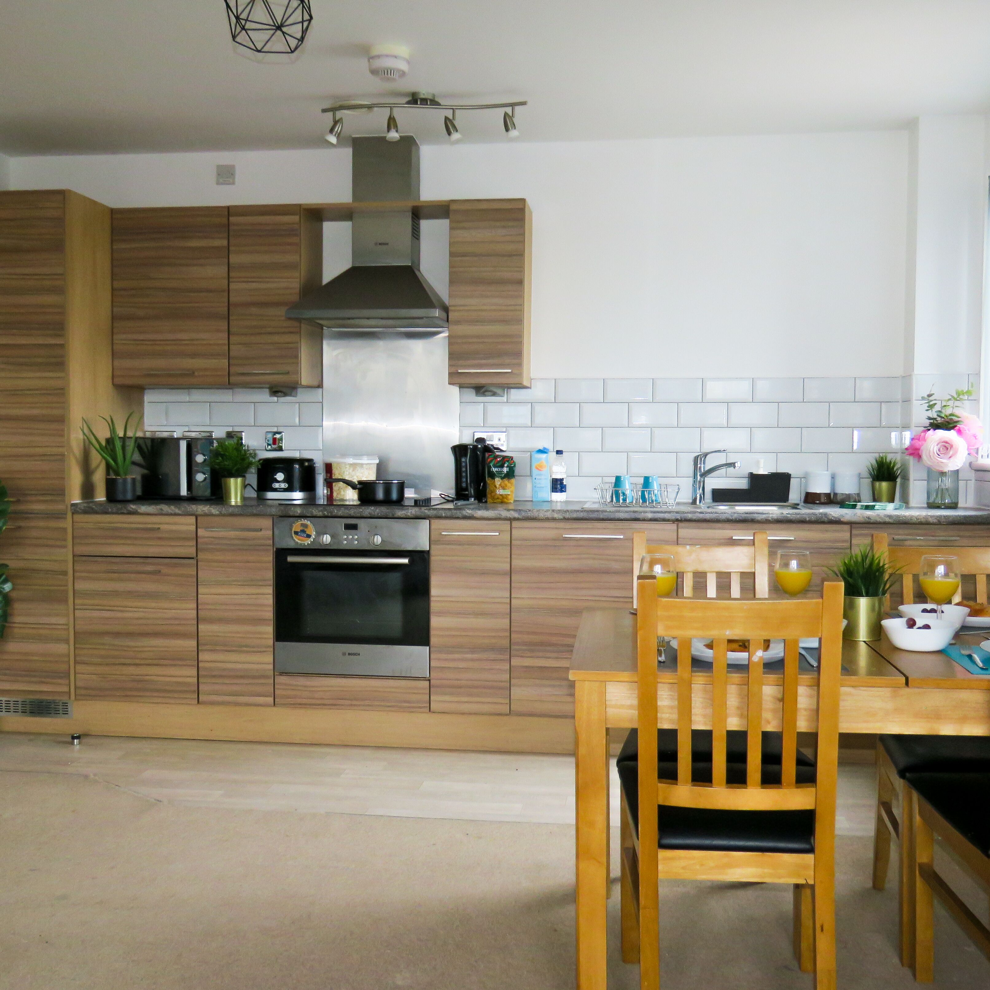 Une cuisine moderne avec des meubles en bois, des appareils électroménagers en acier inoxydable et un coin repas comprenant une table et des chaises en bois.