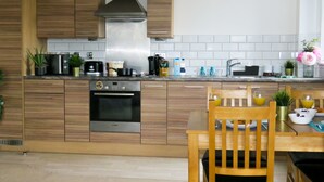 A modern kitchen with wooden cabinets, stainless steel appliances, and a dining area with a wooden table and chairs. - Tudors eSuites Two Bedroom & Balcony (Birmingham)