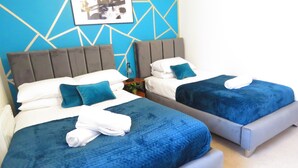 Two beds with blue bedding, a grey headboard, and a blue geometric wall design. - Tudors eSuites Two Bedroom & Balcony (Birmingham)