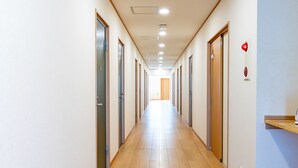 Un pasillo largo y estrecho con suelo de madera y puertas a ambos lados, que conduce a una habitación luminosa al final.