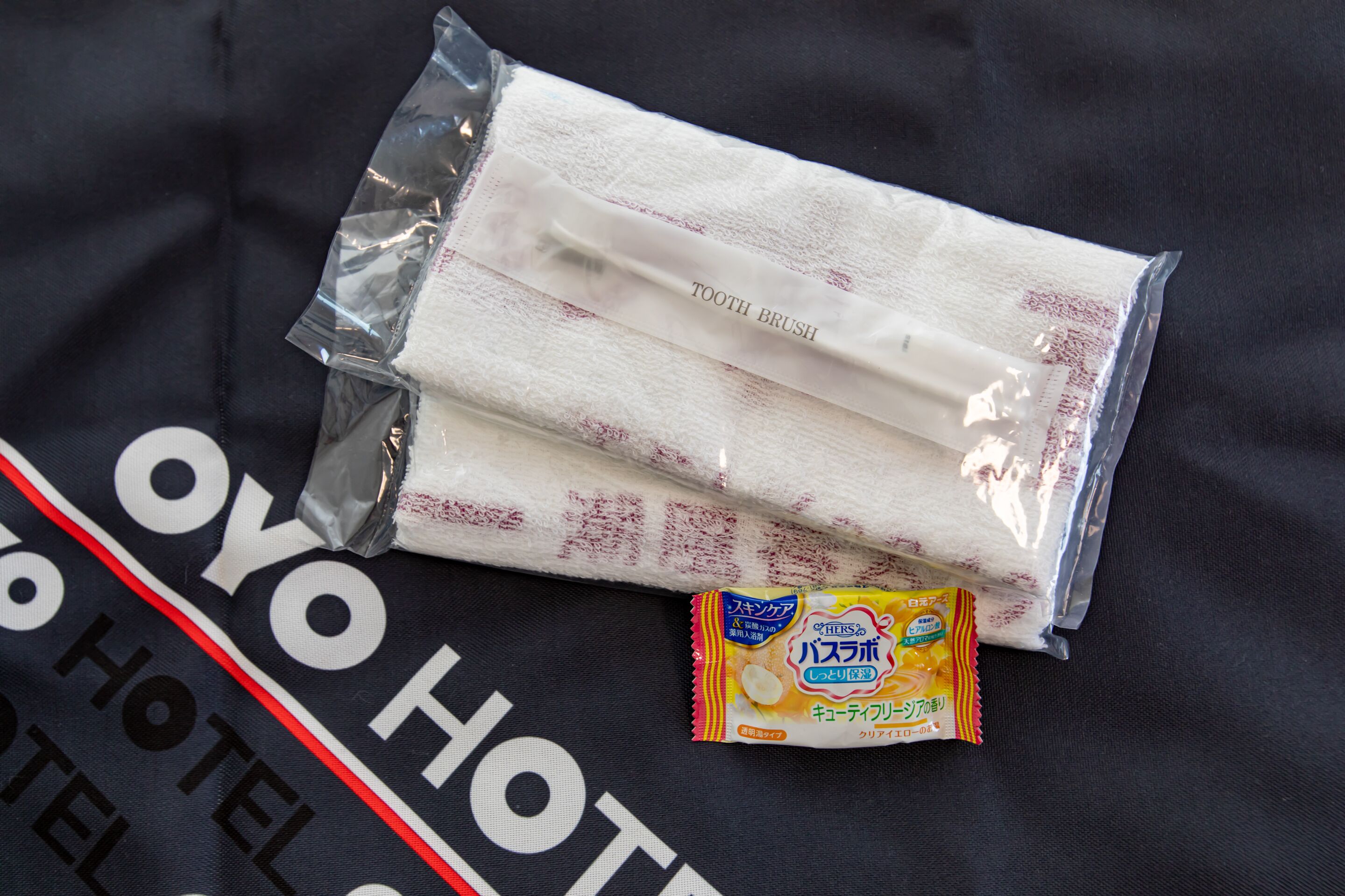 Una toalla de hotel y un paquete de pasta dental sobre un tejido negro con la marca del hotel.