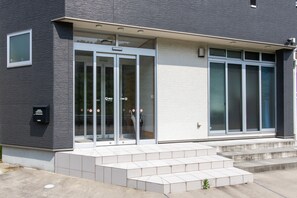 A modern building with a grey exterior, a glass entrance, and a small outdoor area with steps leading up to the entrance. - Tabist Hotel Takagiya Iwaki (Iwaki)