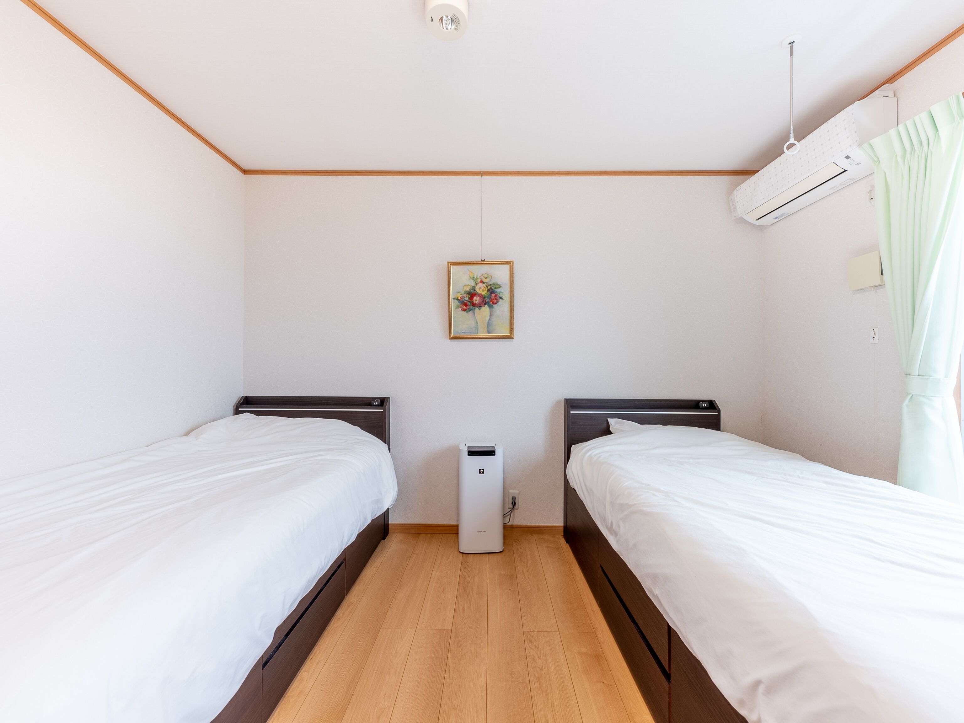 Habitación con dos camas, un equipo de aire acondicionado pequeño y un cuadro en la pared.