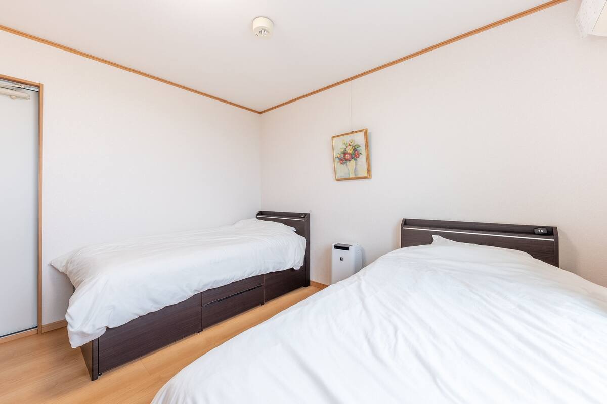 A bedroom with two single beds, wooden flooring, a white ceiling, and a small bedside table with a lamp.
