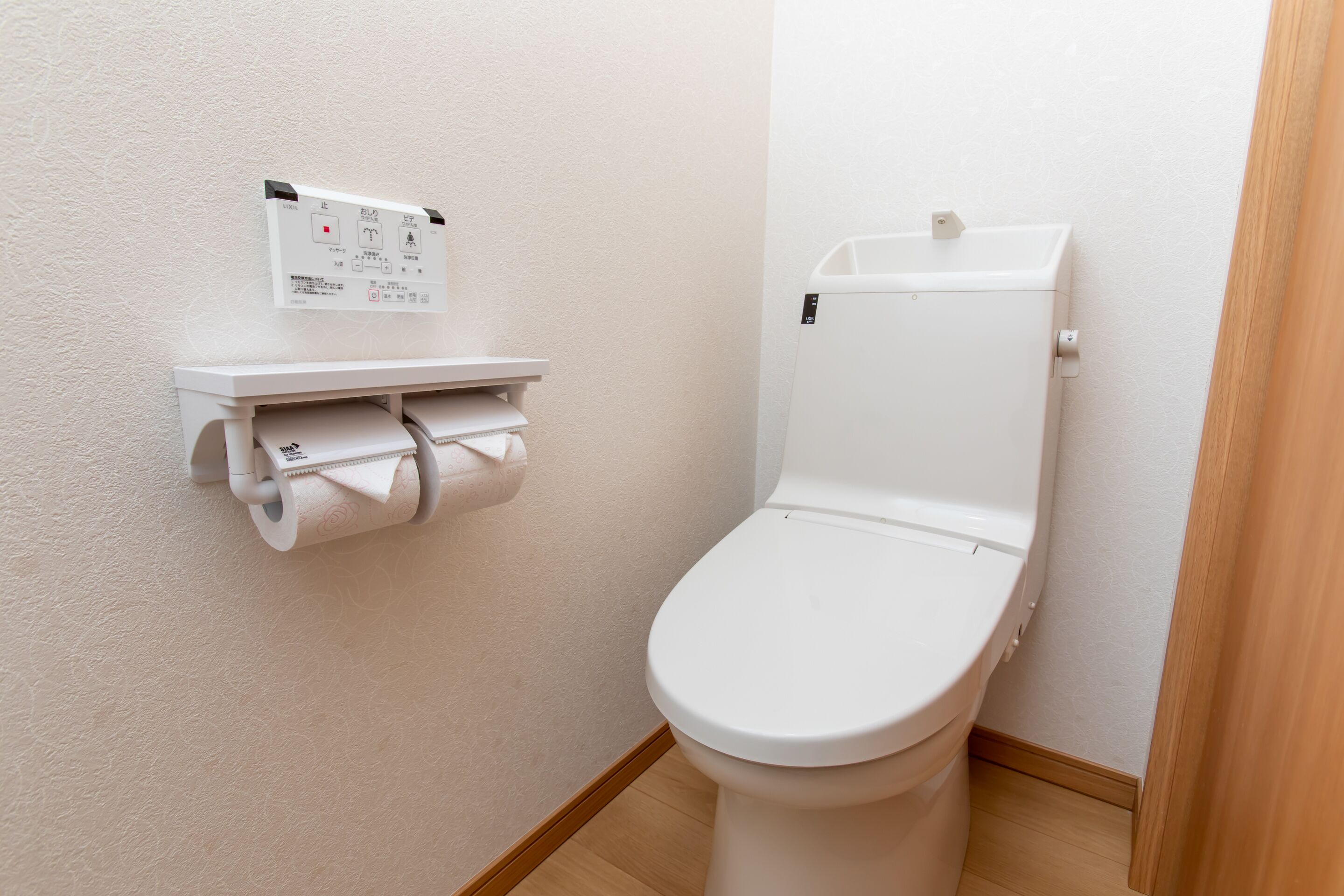 A toilet with a paper towel dispenser and a control panel on the wall.