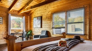 Acogedora habitación tipo cabaña de troncos, con una cama grande, dos ventanas con persianas, una mesita con una planta y un televisor.