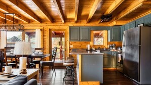 Interior de una cabaña de madera con cocina, comedor y asientos tipo bar.