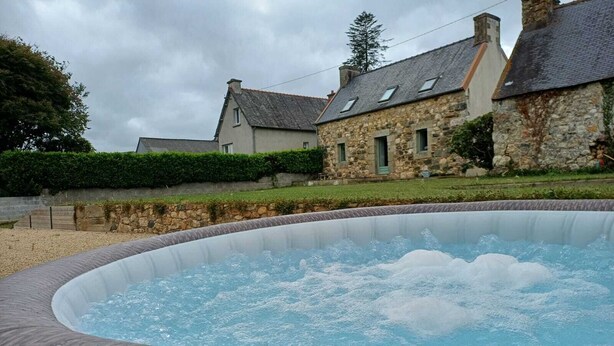 A hot tub in a landscaped area with stone buildings in the background. - Maison Dans une Ancienne Ferme sur 3,5ha (Plougonver)