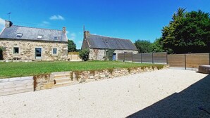 A stone building with a sloped roof, a gravel driveway, and a wooden fence. - Maison Dans une Ancienne Ferme sur 3,5ha (Plougonver)