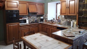 A kitchen with wooden cabinets, a microwave, a stove, and a tiled backsplash. - Maison Dans une Ancienne Ferme sur 3,5ha (Plougonver)