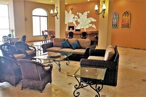 A spacious living area with a large sofa, two armchairs, and a glass coffee table. There are wall-mounted light fixtures and decorative wall art.