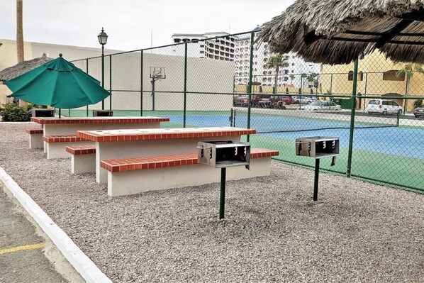 A sports court with a fence, benches, and a thatched roof structure.