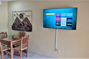 A flat-screen TV mounted on a wall displaying a Roku TV interface with streaming options like Netflix, YouTube, and vevo.