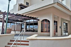 A building with a covered patio area, a staircase, and large windows.