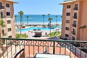 A resort with a central pool area, palm trees, and a view of the ocean.