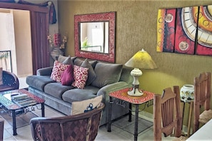 A living room with a sofa, patterned cushions, a coffee table, a side table with a lamp, and a decorative mirror.