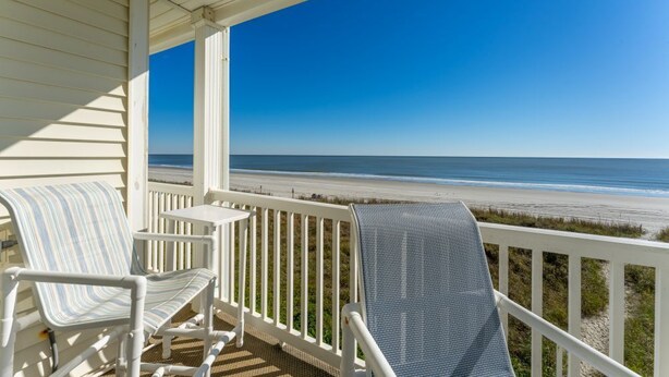A porch with two rocking chairs and a small table, overlooking a beach. - Charming Ocean-view Condo at Ocean Pier 3 (North Myrtle Beach)