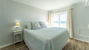 A bedroom with a bed, a nightstand, a lamp, and a window with curtains. - Charming Ocean-view Condo at Ocean Pier 3 (North Myrtle Beach)