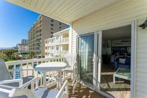 Relax on the balcony with a round table and two chairs, overlooking the pool area with lounge chairs and umbrellas.