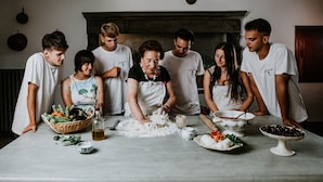 Um grupo de pessoas reunido em volta de uma mesa na cozinha, preparando comida.