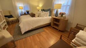 Ein ordentlich eingerichtetes Schlafzimmer mit einem großen Bett, Nachttischen, einem Sessel und einem kleinen Tisch mit einer Lampe.