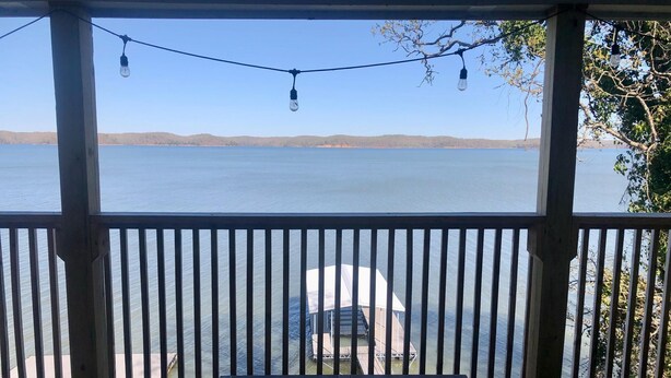 Eine Holzterrasse mit Tisch und Stühlen mit Blick auf ein Gewässer, mit einem Steg und einem Boot.