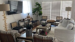 Ein Wohnzimmer mit einer Couch, Sesseln, einem Couchtisch, einem Fernseher und einem Deckenventilator.