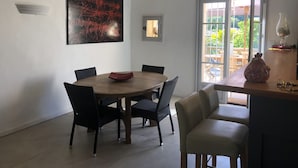 A dining area with a wooden table and chairs, a large abstract painting, a clock, and a view of the outdoors through a glass door.